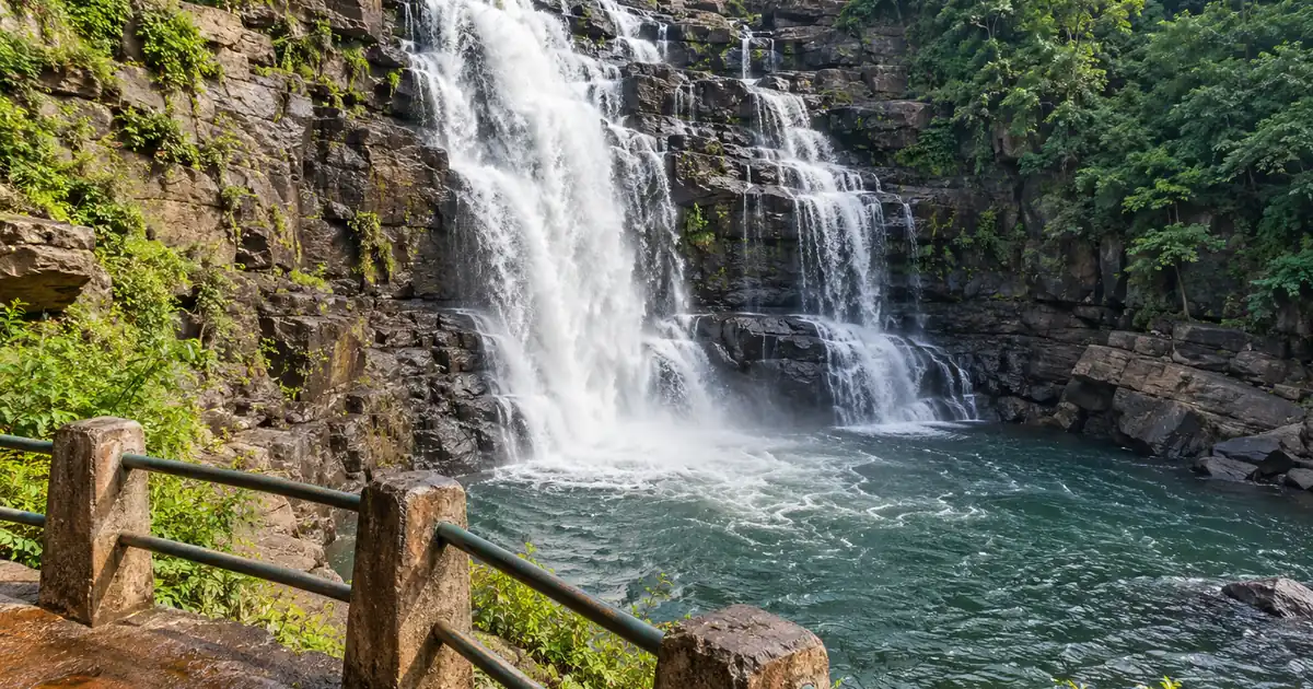 Pradhanpat Waterfall cascading over dark rock beside a safe viewing railing