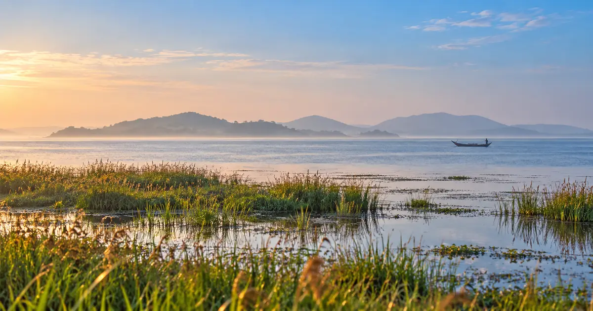 A wooden boat crosses Chilika Lagoon beneath distant hills at sunrise