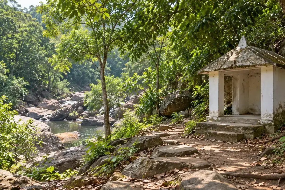 A small white shrine beside a shaded forest path and rocky stream