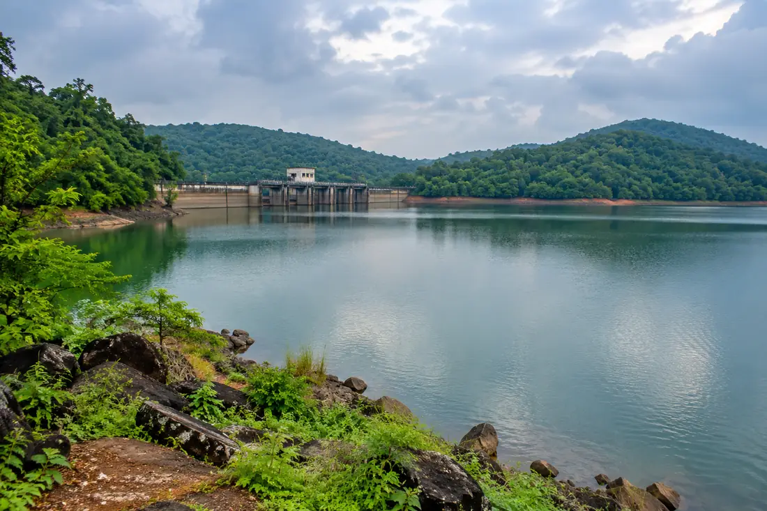 Calm water fills Mandira reservoir beneath forested hills